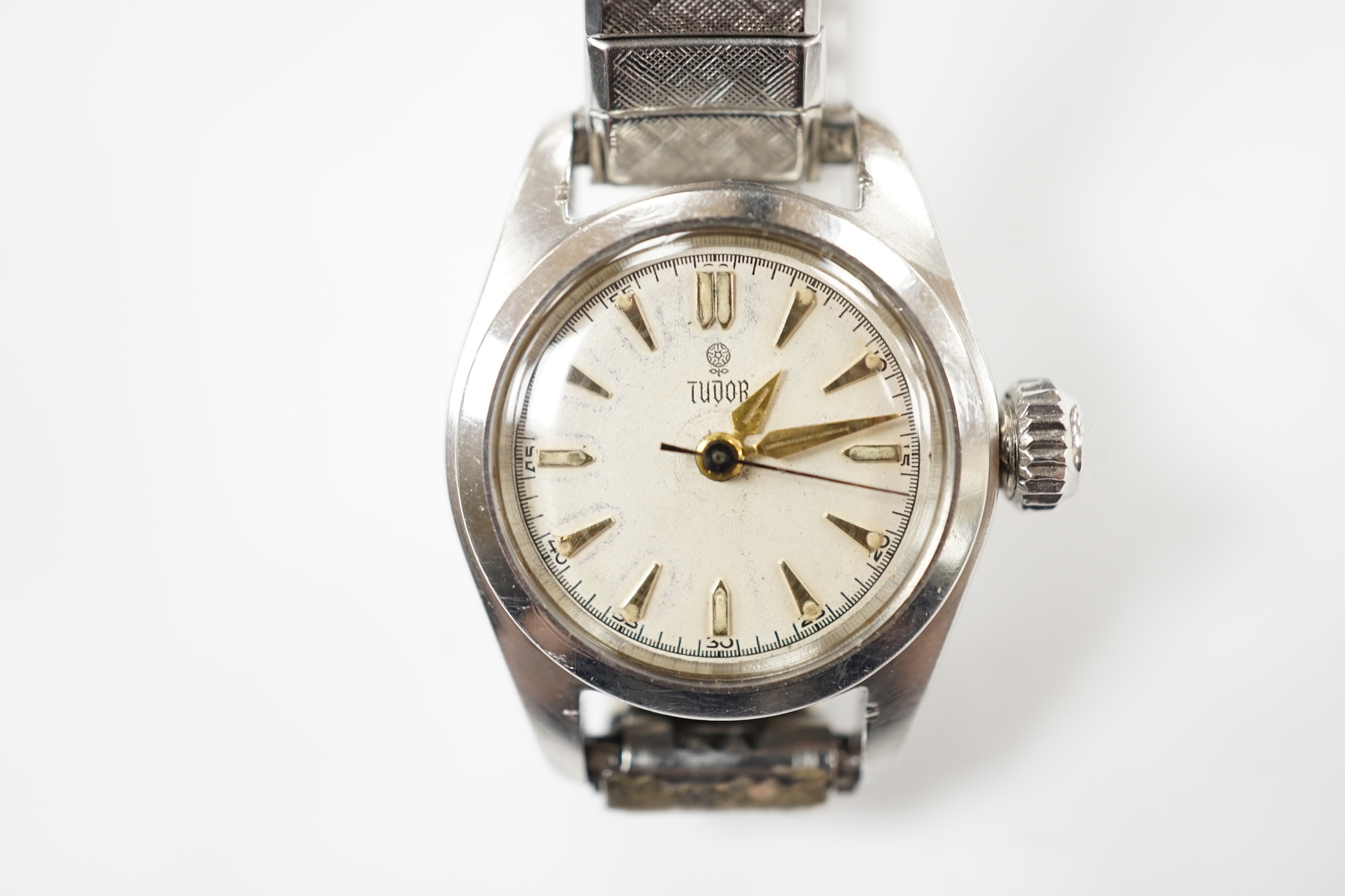 A lady's stainless steel Tudor manual wind wrist watch, with baton numerals, on an associated flexible bracelet.